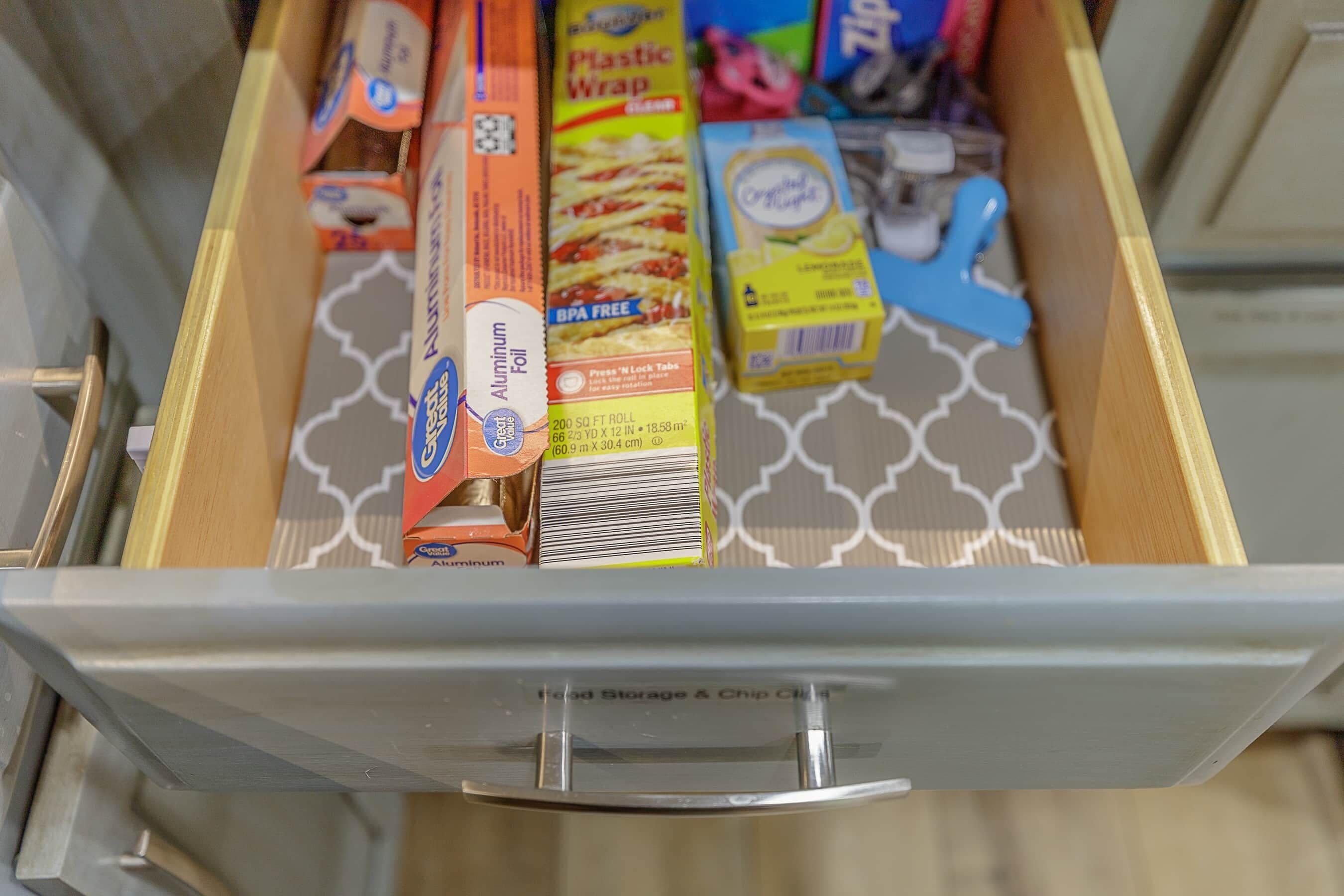 A drawer containing various food items including aluminum foil, plastic wrap, and a blue plastic bag.