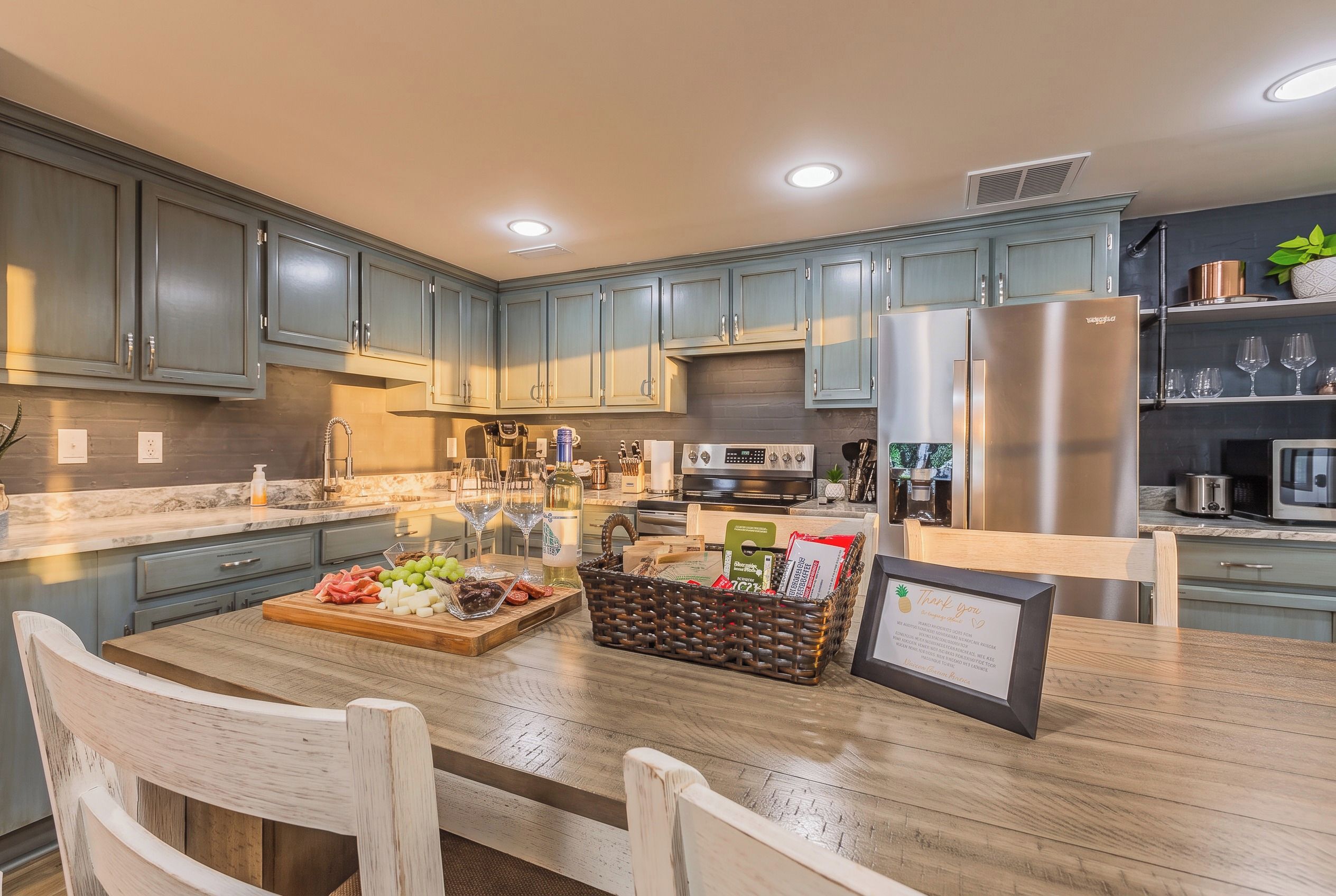 A modern kitchen with grey cabinets, stainless steel appliances, and a wooden dining table set for a meal.