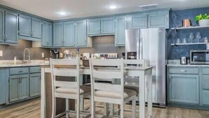 A kitchen with blue cabinets, a white refrigerator, and a wooden dining table with chairs.