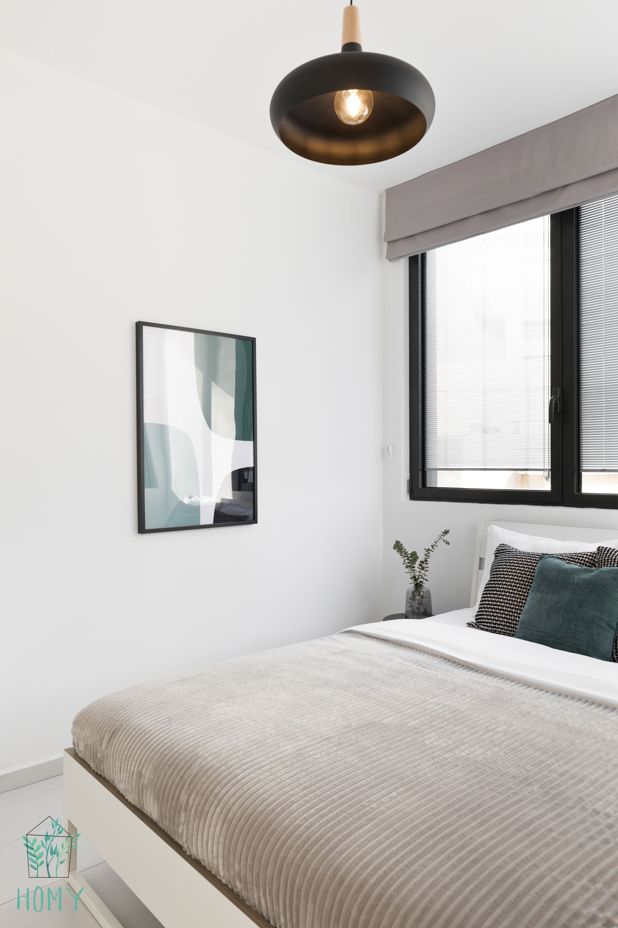 A modern bedroom with a bed, a hanging light fixture, a window with blinds, and a framed abstract artwork on the wall.