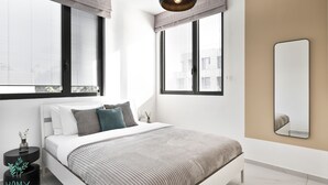 Een moderne slaapkamer met een bed, nachtkastjes, een spiegel en grote ramen.