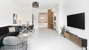 Een moderne woonkamer met een zwarte bank, een eettafel en een aan de muur bevestigde televisie.