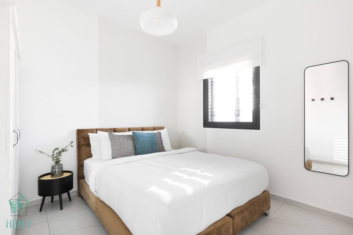 A modern bedroom with a bed, bedside table, and a mirror.