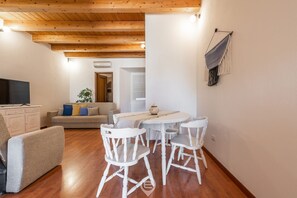 A cozy living area with a wooden ceiling, a sofa, a TV, and a dining table with chairs.