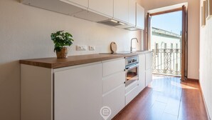 Una cocina moderna con armarios blancos, encimera de madera y horno empotrado. Hay una planta en la encimera y se ve un balcón con barandilla de metal.