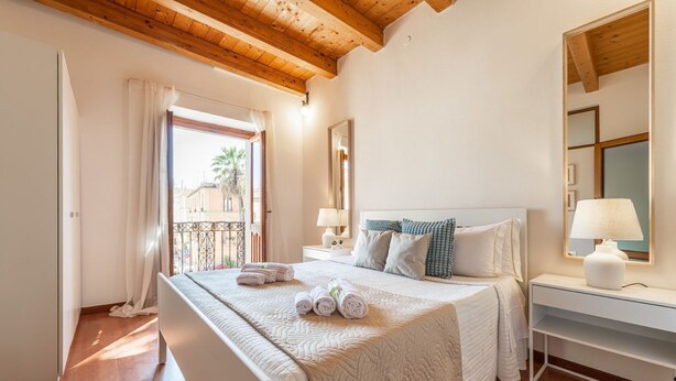 Un dormitorio con techo de madera, una cama con ropa de cama blanca, una mesita de noche, una lámpara y vistas al exterior.