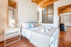 A bedroom with a bed, bedside tables, a mirror, and a large window.