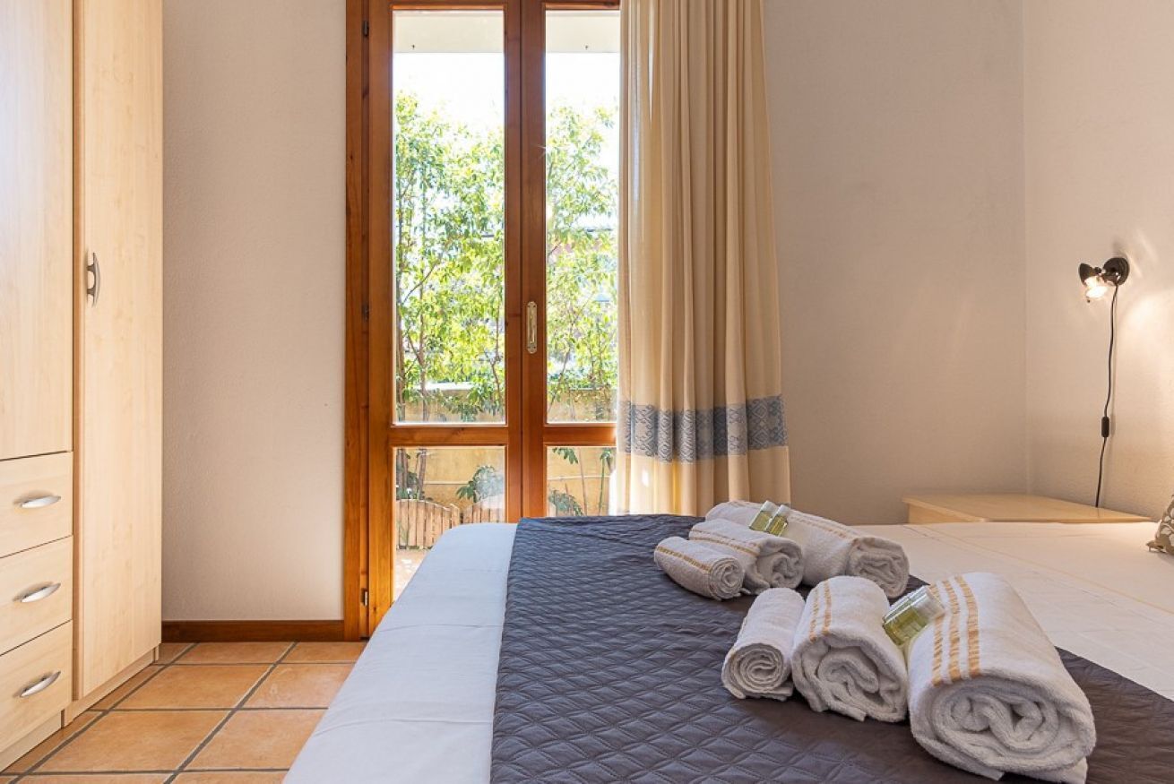 Hotelkamer met groot bed, houten garderobe, nachtkastje en uitzicht op groen door een glazen deur.