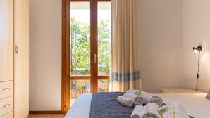 Habitación de hotel con una cama grande, un armario de madera, una mesita de noche y vistas a zonas verdes a través de un ventanal.
