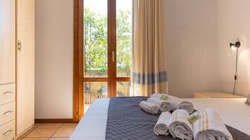 Hotelkamer met groot bed, houten garderobe, nachtkastje en uitzicht op groen door een glazen deur.