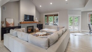 A modern living room with a sectional sofa, a fireplace, a flat-screen TV, and a large window offering a view of the outdoors. - Family Friendly w/ Suncadia Pool Access (Cle Elum)