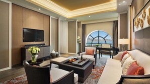 Une chambre d’hôtel moderne dotée d’une télévision à écran plat, de sièges confortables, d’un coin repas et d’une grande fenêtre offrant une vue sur la mer.