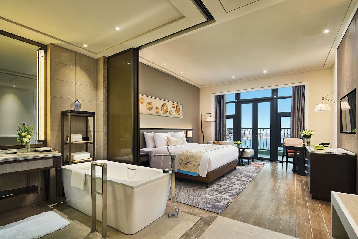 Habitación de hotel moderna con una cama grande, baño independiente, escritorio y balcón con vistas.