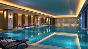 Une piscine intérieure moderne, dotée de chaises longues et de luminaires fixés au mur.