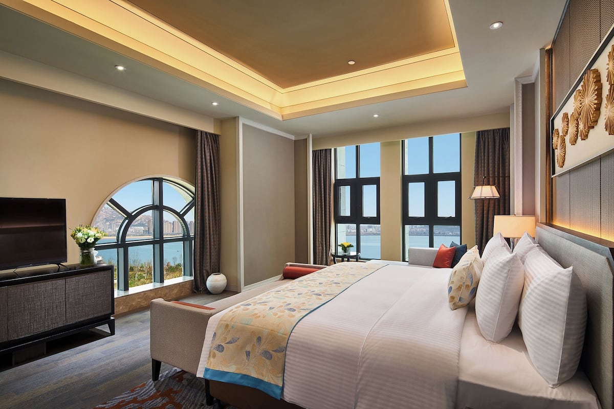 Una habitación de hotel con una cama grande, un televisor y vistas de la ciudad a través de amplios ventanales.
