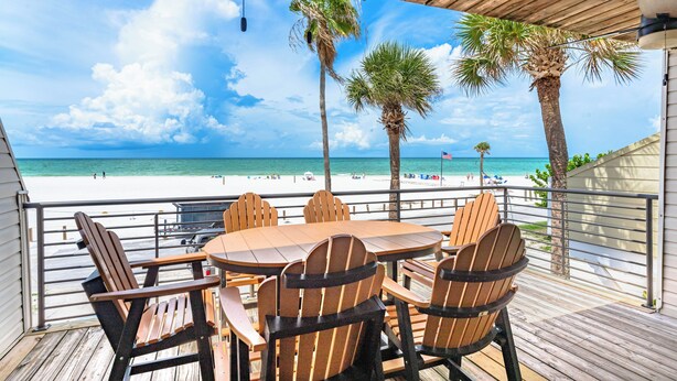 Une terrasse en bois avec une table et des chaises donnant sur une plage.