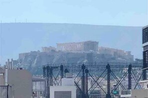 A view of a building with a prominent structure resembling the Parthenon in the background, suggesting a historical or cultural significance. - Fab New Flat in Central Athens w/ Acropolis Views (Athina)