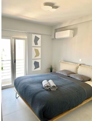 Relax in a serene bedroom with a large bed, sliding glass door to an outdoor area, and a ceiling-mounted air conditioning unit.