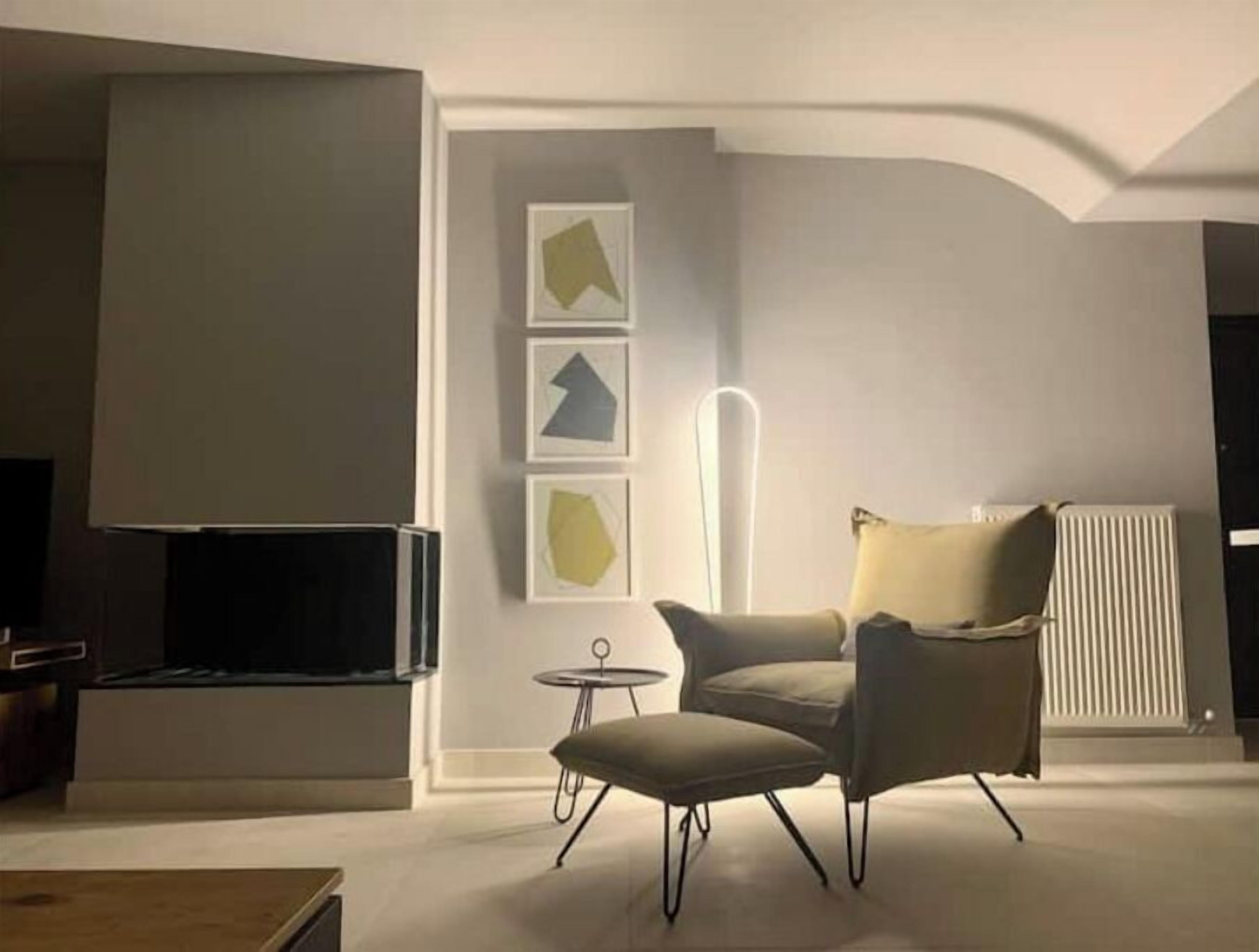 Ein modernes Wohnzimmer mit Flachbildfernseher, einem bequemen Sessel, einem kleinen runden Tisch und abstrakten Wandbildern.