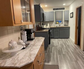 A kitchen with marble countertops, wooden cabinets, and a grey backsplash.