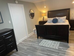 A bedroom with a dark wood bed, a bedside table with a lamp, a dresser, and a patterned rug.