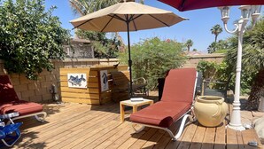 Eine Holzterrasse mit einem roten Liegestuhl, einem Holztisch und einem großen Blumentopf.