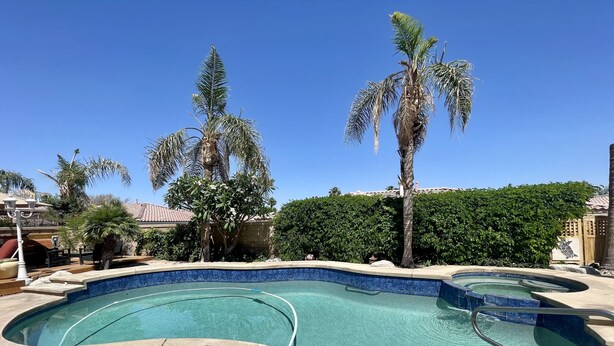 Ein Swimmingpool mit Kiesbord, Palmen und blauem Himmel.