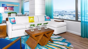 Un salon moderne avec un canapé blanc, des coussins bleus et jaunes, une table basse en bois et une vue sur la ville grâce à de grandes fenêtres.