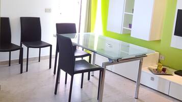 A modern living room with a glass dining table, black chairs, a red sofa, and a green accent wall.