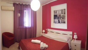 A hotel room with a red bedspread, a white headboard, a red chair, a white nightstand, and a poster of the City of London on the wall. - Residence Eloisa  (Balestrate)