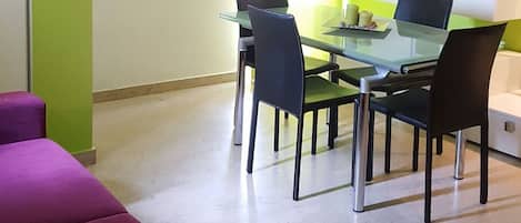 A dining area with a glass table and chairs, a clock on the wall, and a green accent wall.