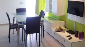A modern living room with a dining area, a flat-screen TV mounted on the wall, and a window with curtains. - Residence Eloisa  (Balestrate)