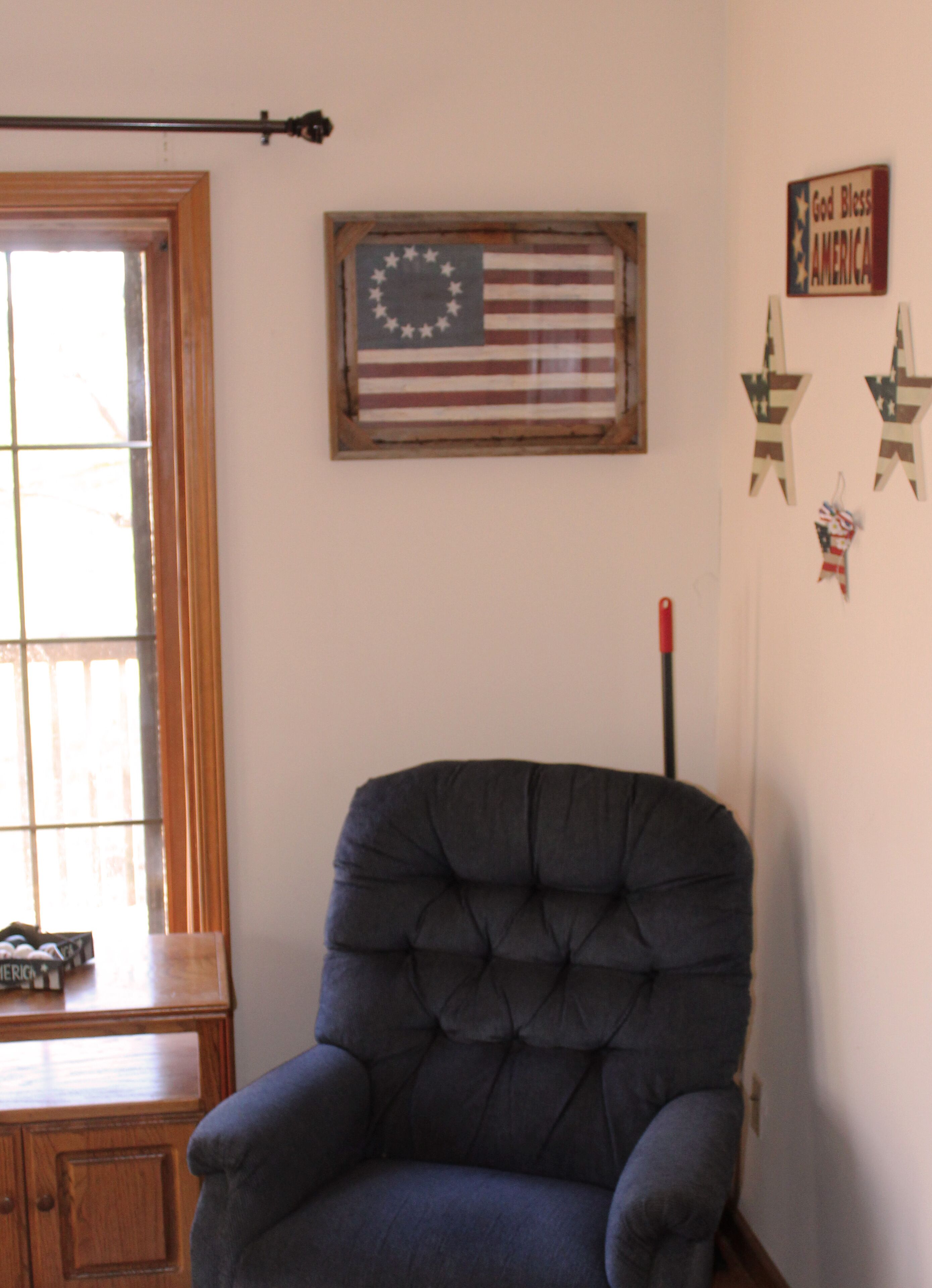 Une pièce avec une grande fenêtre, un fauteuil bleu et des drapeaux américains accrochés au mur.