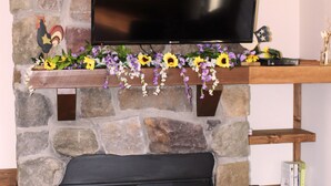 Una chimenea de piedra con un televisor de pantalla plana montado encima, un fuste decorado con flores, y una estantería a la derecha.