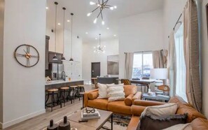 Relax in a spacious living area with a sofa and coffee table, adjacent to a kitchen with bar stools and a large clock.