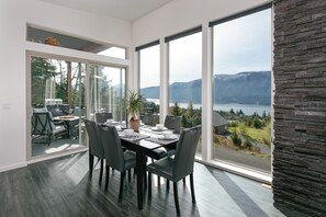 A modern dining area with a large table, chairs, and a view of a lake and mountains. - Epic Columbia River views * New Modern Home in the heart of the gorge. (Carson)