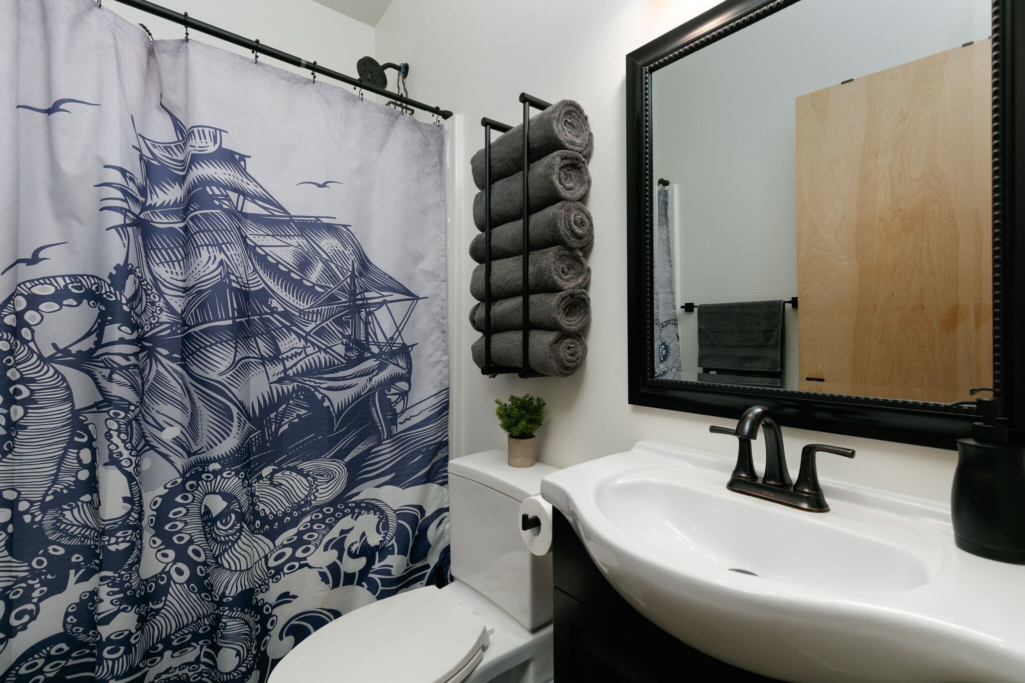 A bathroom with a white sink, a mirror, and a towel rack with rolled towels.