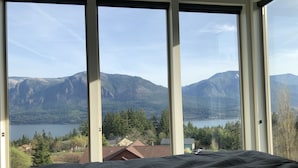 Ein Schlafzimmer mit großem Fenster und Blick auf einen See und Berge.