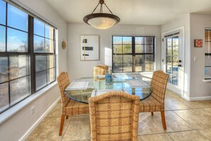 A dining area with a glass table surrounded by wicker chairs, large windows, and a ceiling light fixture.