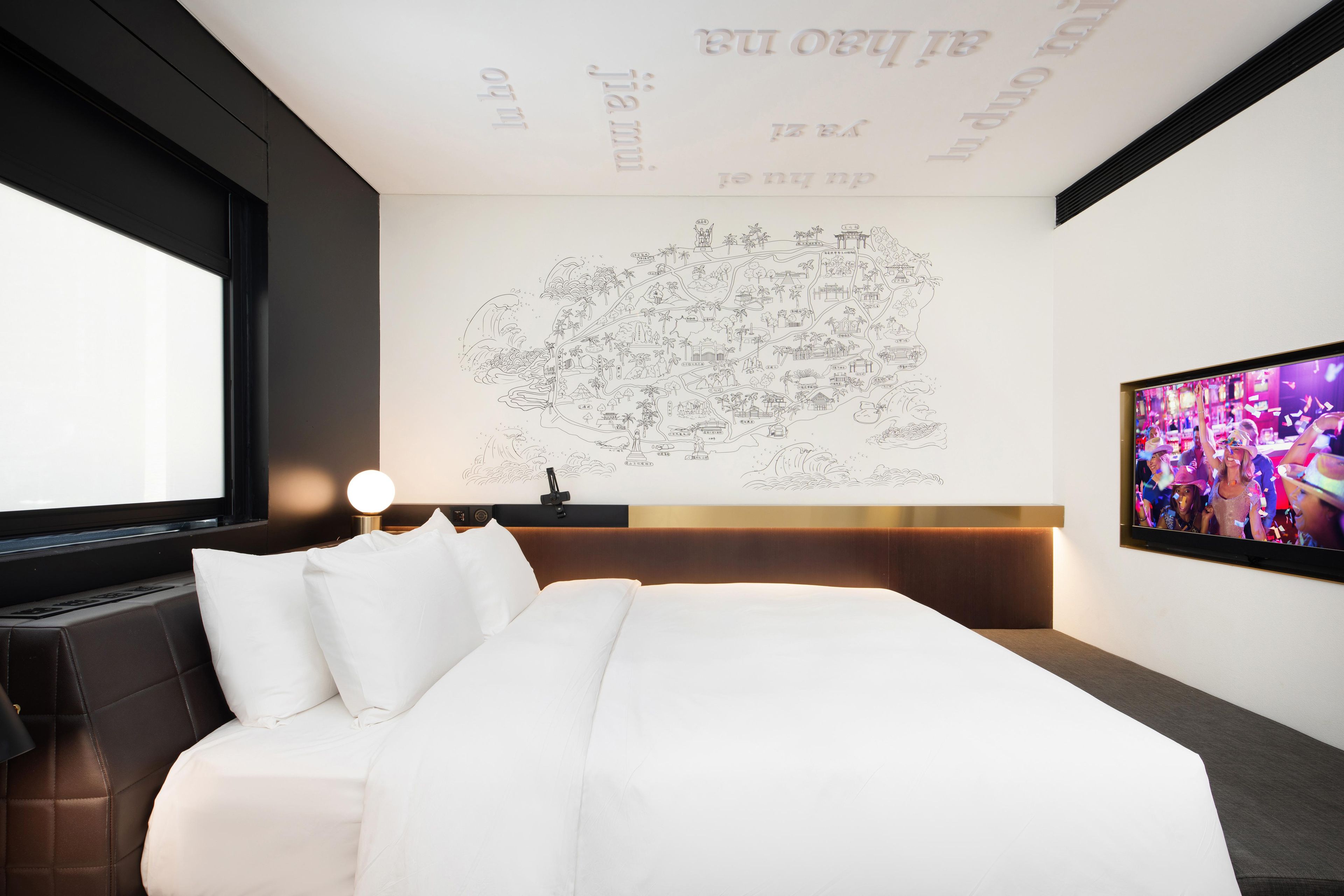 A modern hotel room with a large bed, a flat-screen TV, and a wall with a map.