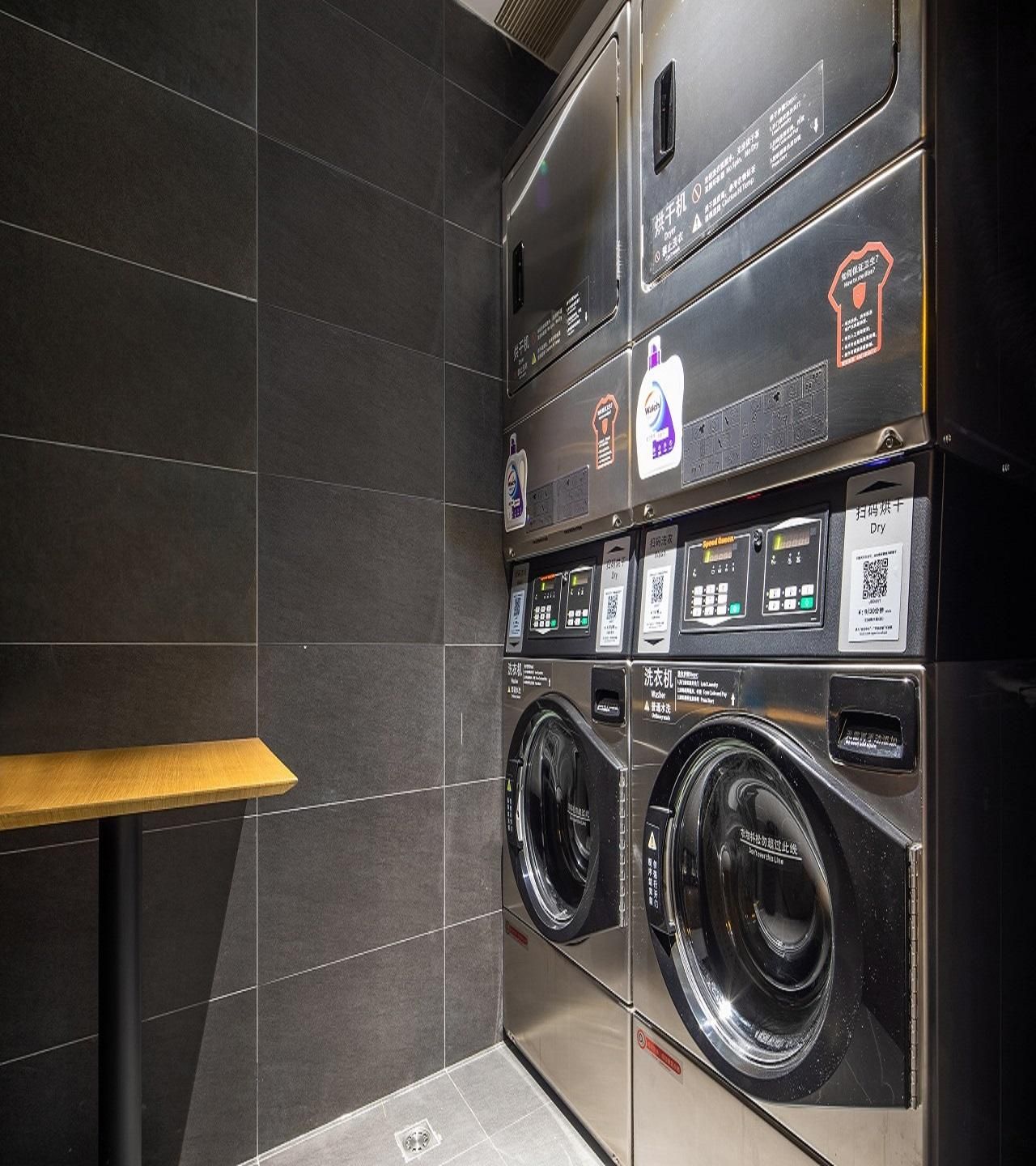 A modern laundry facility with multiple washing machines and dryers, equipped with digital controls and safety instructions.