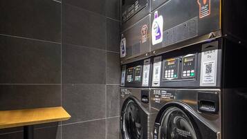 A modern laundry facility with multiple washing machines and dryers, equipped with digital controls and safety instructions.