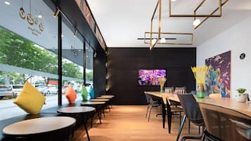 A modern cafe interior with round tables, black chairs, and a large TV screen on the wall.