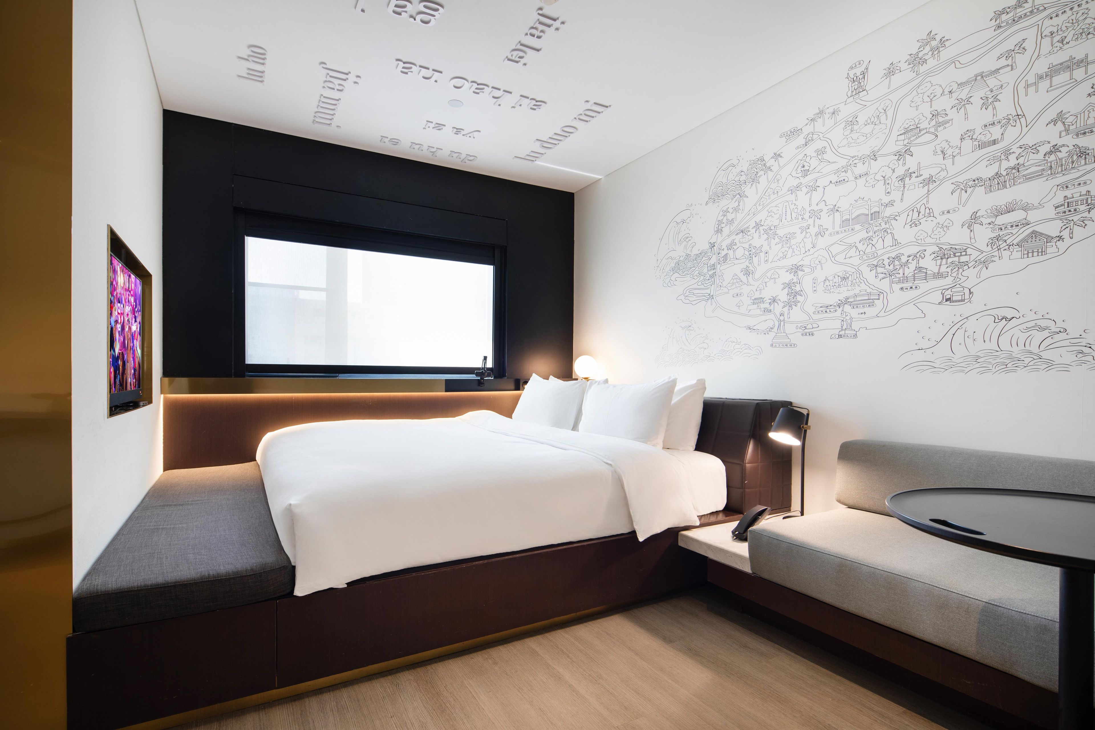 Una habitación de hotel moderna con una cama grande, zona de estar, ventana y una pared con un mapa.