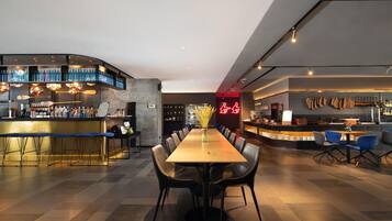 A modern restaurant with a bar area, a long dining table with chairs, and a neon sign.