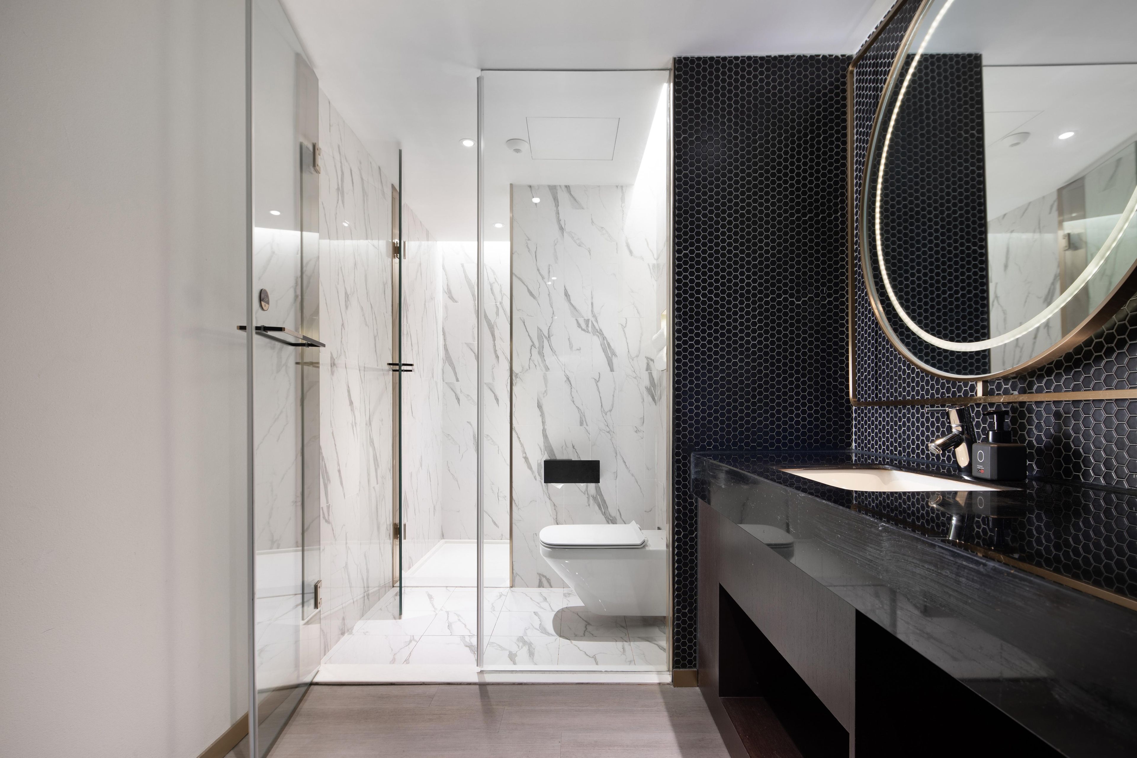 A modern bathroom with a glass-enclosed shower, a black tiled wall, and a large mirror.