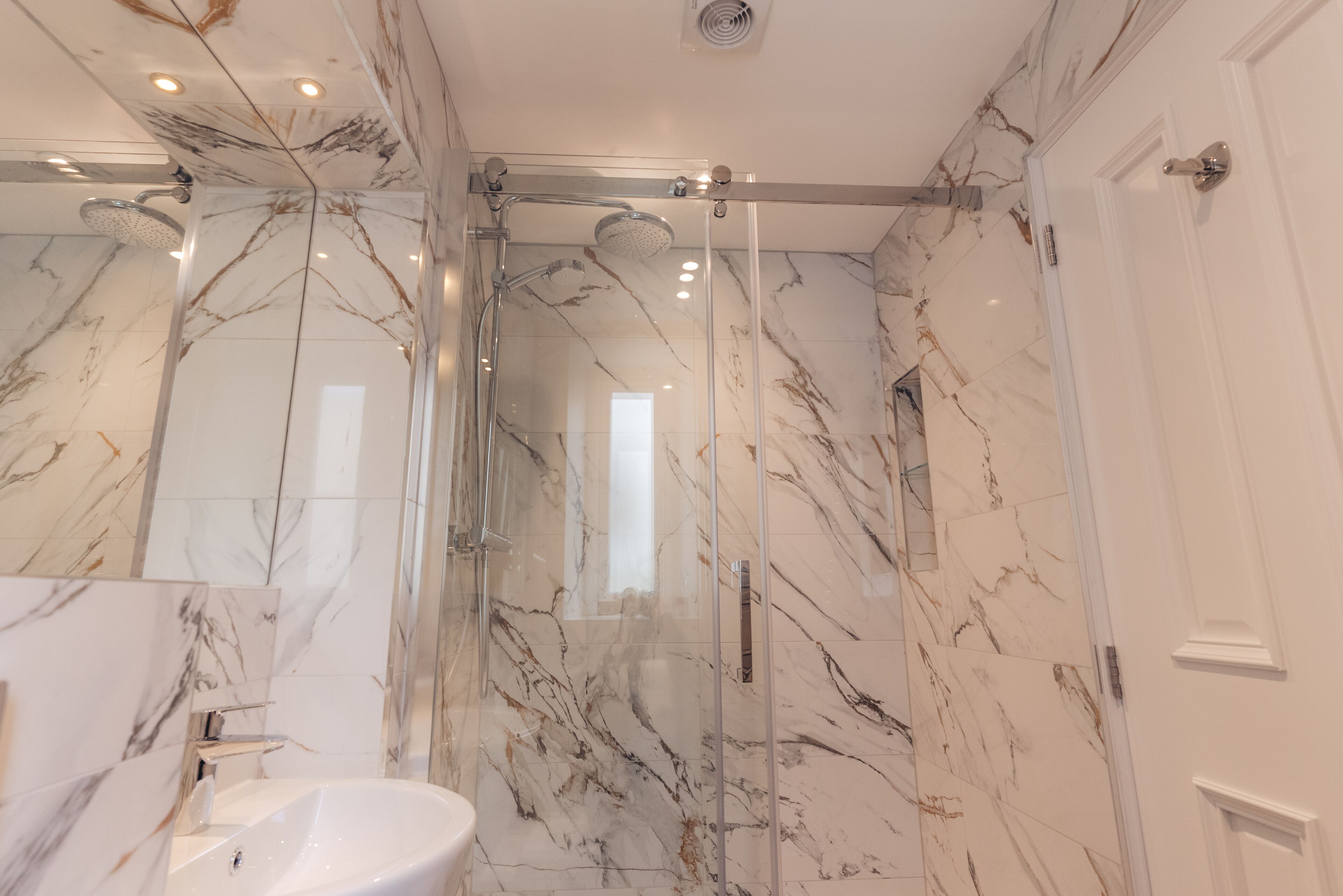A modern bathroom with a glass-enclosed shower, marble walls, and a white sink.