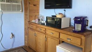 Una cocina con armarios de madera, microondas, cafetera y televisor montado en la pared.