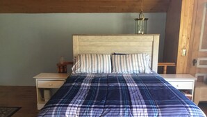 Un dormitorio con cabecera de madera, colcha escocesa, dos mesitas de noche y una lámpara colgante.