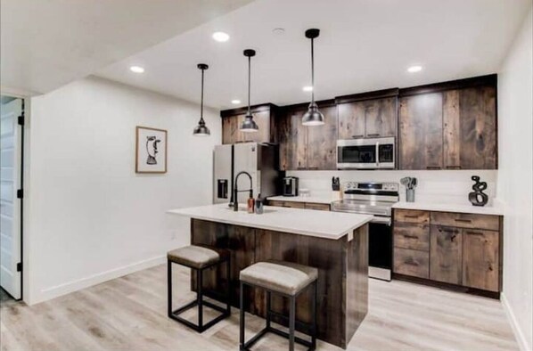 Enjoy cooking in this well-equipped kitchen with a central island and barstools, featuring a refrigerator, microwave, and stove.